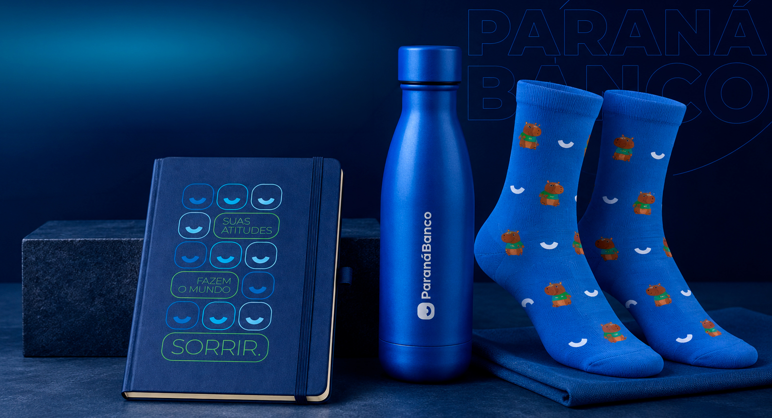 Produtos do kit onboarding Paraná Banco: caderno personalizado, garrafa e meia de capivara